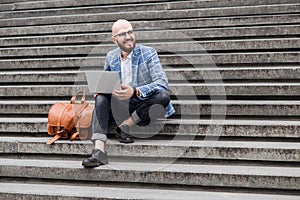 Young man with a leather bag sits on the stairs