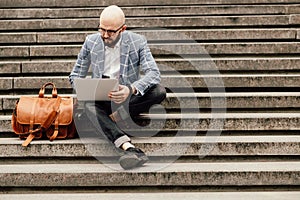 Young man with a leather bag sits on the stairs