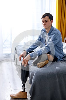 young man leg amputee wearing or changing prostheses at home sitting on bed