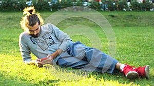 Young man lies on the grass, looks into a smartphone, checks social networks. Concept. Caucasian man relaxing in the