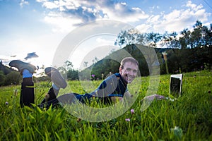 Young man lies on green grass with laptop and working