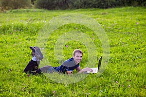 Young man lies on green grass with laptop and working