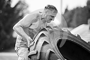 Young man lift up big heavy wheel on competition