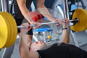 Young man lifting the barbell in gym with instructor