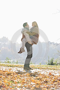 Young man lifting woman in park during autumn