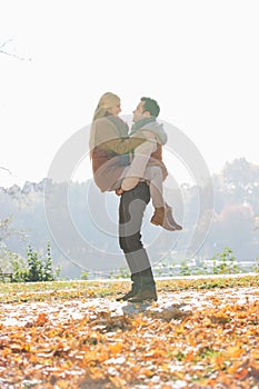 Young man lifting woman in park during autumn