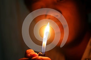 A young man lighting a match in hand on dark background.