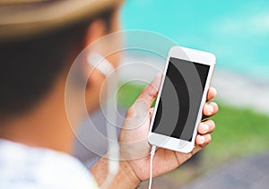 Young man listen music on smartphone while sitting near swimming pool. Relax concept.