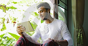 Young Man Listen To Music On Tablet Computer With Earphones Sing Sitting One On Window Sill