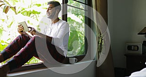 Young Man Listen To Music On Tablet Computer With Earphones Sitting One On Window Sill