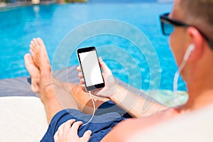 Man listening to music and holding mobile phone in hand by the pool.