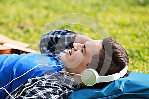 Young man listening to music while lying on green grass in park