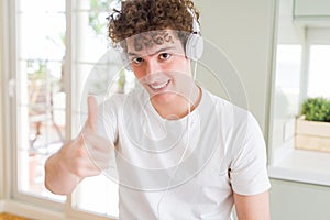 Young man listening to music wearing headphones at homes doing happy thumbs up gesture with hand