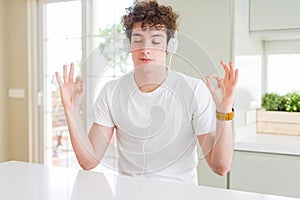 Young man listening to music wearing headphones at homes relax and smiling with eyes closed doing meditation gesture with fingers