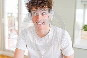 Young man listening to music wearing headphones at homes smiling looking side and staring away thinking