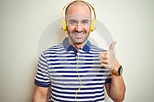 Young man listening to music wearing yellow headphones over isolated background doing happy thumbs up gesture with hand