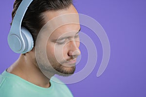 Young man listening to music with wireless headphones, guy smiling in studio on purple background. radio concept.