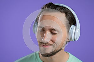 Young man listening to music with wireless headphones, guy smiling in studio on purple background. radio concept.
