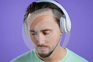 Young man listening to music with wireless headphones, guy smiling in studio on purple background. radio concept.