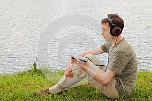 Young man listens music sits on ashore