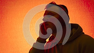 A young man listens to music with headphones on an orange background.