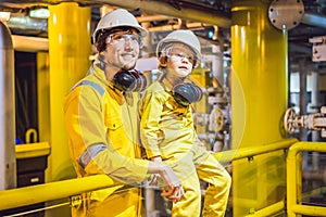 Young man and a little boy are both in a yellow work uniform, glasses, and helmet in an industrial environment, oil