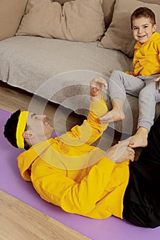 Young man with little boy doing fitness exercises at home. Father and son having fun during sport. Dad and his child