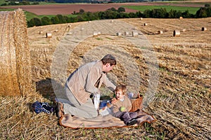 Young man and little boy making picnic on hay field