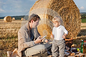 Young man and little boy making picnic on hay field