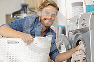 young man loading clothes into washing machine in kitchen