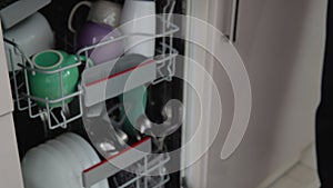 Young man loading dirty dishes into a dishwasher machine. A man uses modern appliance to keep the home clean. Close-up