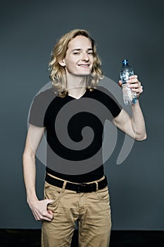 A young man with long blond hair drinks clean water from a bottle, quenches thirst