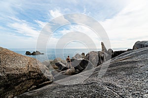 Young Man with a long hair in a white t-shirt, standing on a rock and enjoying a view on a sea. Traveling.