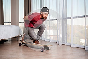 A young man on a longboard, imagining that he is driving down the street. Indoor. Concept of quarantine and activity at home. Copy