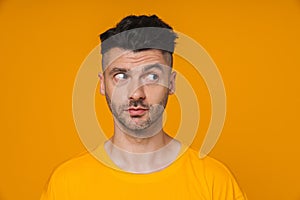 Young man looking away while standing isolated over yellow background