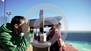 Young man looking through binoculars at observation deck, admiring sea horizon