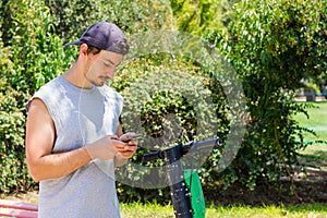 Young man looking at cellphone with electric scooter at park