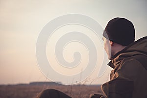 Young man looking into the distance at dawn in rural field. The light illuminates his face.