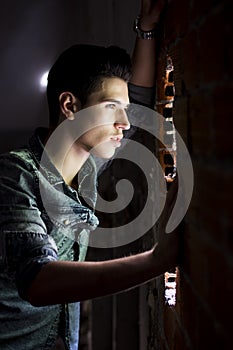 Young man looking through hole in brick wall