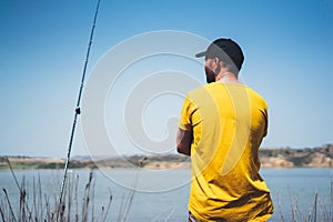 Young man looking on horizont seascape and holds a fishing rod and catches fish in the nature background, hipster fisherman spends