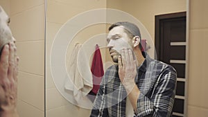 Young man looking in mirror touch his face before shave in bathroom. Slow motion