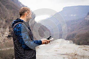 Young man looking at a navigator gps on the bank of a mountain river laying a route while traveling