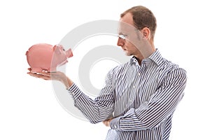 Young man looking at pink piggy bank isolated on white background