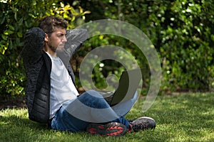 Young man looking at the screen of his computer with his hands behind his head like he is relaxing.