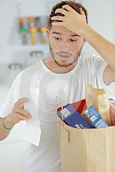 young man looking with shock at shopping receipt