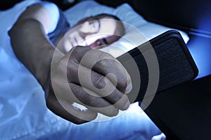 Young man looking at the smartphone in bed at night