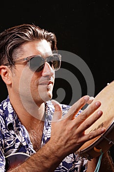 Young man looking to the side, playing the pandeiro, with black sunglasses and blue and white hawaiian shirt