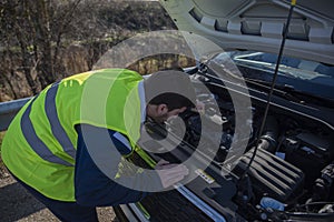 Young man looking under the hood of a broken down car