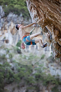 Young man looking up while climbing challenging route on cliff