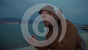 A young man looks into the theophone against the background of the sea.